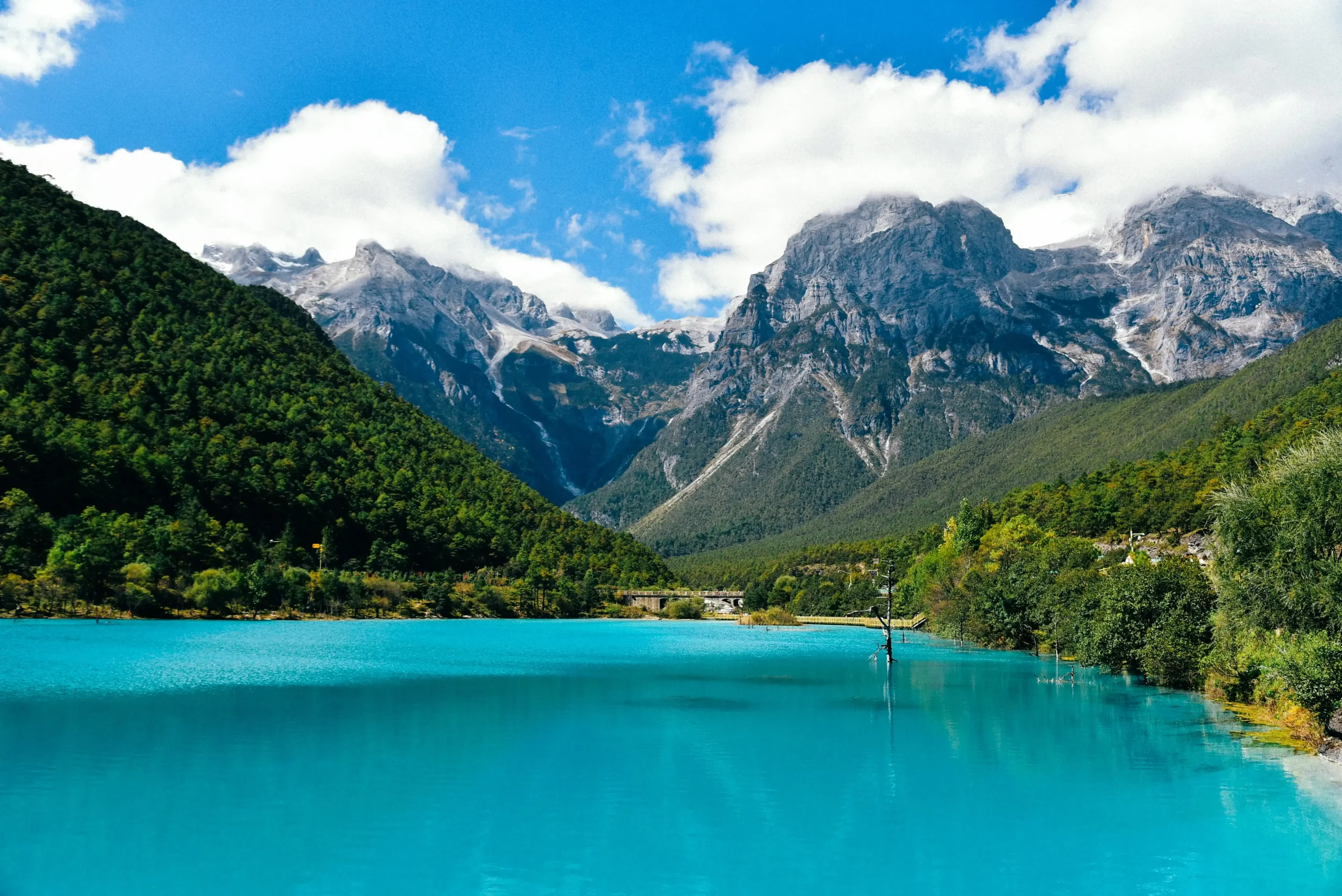 Turquoise alpine lake reflecting snow-capped mountain peaks surrounded by autumn foliage under a clear blue sky.