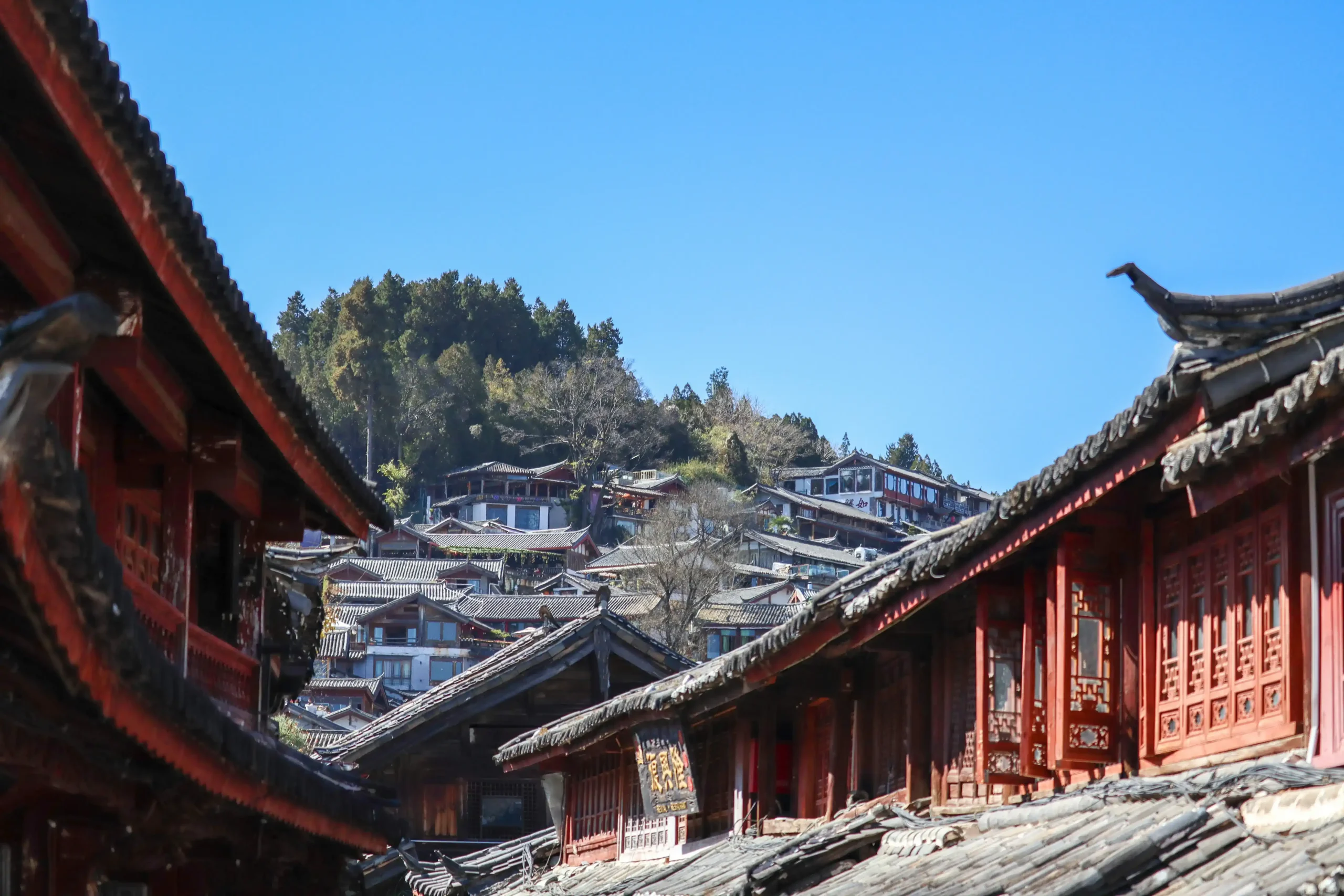 A close-up view of traditional tiled wooden eaves and rooftops of ancient buildings nestled in Lijiang Old Town under a clear sky.
